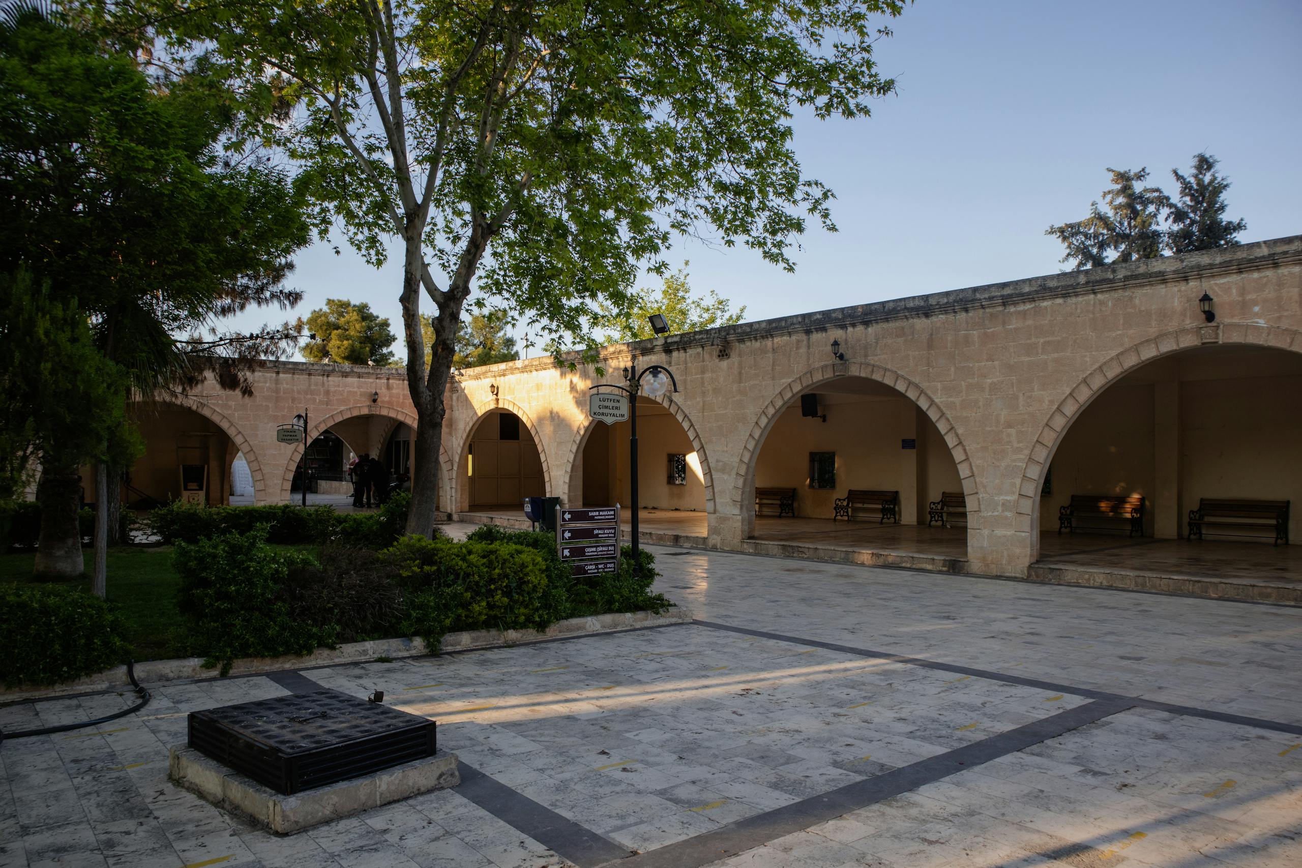 Peaceful courtyard in Şanlıurfa, Türkiye, featuring historical stone arches and lush greenery.
